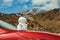 Base of volcano Teide. Snowman on on the hood of the red car. Peack of Teide with white snow spots, partly covered by the clouds.