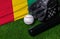 Baseball bat, glove and ball near Guinea flag on green grass background