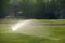 Baseball field sprinkler waters the grass, pointed right on a sunny day