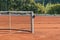 Baseline and net of an empty clay tennis court on a sunny day