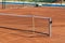 Baseline and net of an empty clay tennis court on a sunny day