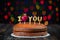 Basic cake with I love you candles, heart, placed on a vintage table and coloured bokeh patterns in the background.