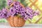 Basket with a bouquet of lilac flowers on a white wooden table in the summerhouse in the garden