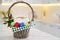 Basket with delicious Easter cake and dyed eggs on white table in kitchen. Space for text