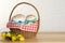 Basket with delicious Easter cakes, dyed eggs and flowers on wooden table. Space for text