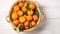 Basket full of fresh whole juicy clementine oranges with leaves on white wooden textured table. Top view, copy space, Generative