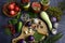 Basket with tomatoes, cutting board with garlic, eggplant, hot pepper, knife, jars and seasonings on a dark background