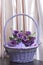 A basket, woven from a vine, filled with gifts and flowers. On a light background.