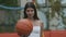 Basketball ball in slim female Caucasian hand with blurred beautiful brunette sportswoman smiling at the background