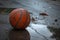A basketball sits on the wet ground during a rain shower, soaking in the water droplets, A well worn basketball laying alone in a