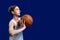 Basketball and teenager. The guy in the white jacket can throw a ball from the chest. Isolated on blue background. Copy space.