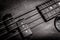 Bass guitar with four strings in black and white closeup. Detail of popular rock musical instrument. Vintage style photo of bass