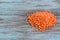 Batch of orange lentils scattered on light wooden background