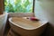 Bath near window with tropic greenery for relax. Luxury round bath tub with jungle view. Spa,organic and skin care