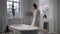 Bathrobe model entering bath room. Calm lady touching foam preparing spa at home