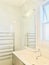 Bathroom corner with a marble wall, a light above the mirror and a towel rail,  a window above the wash basin.