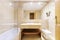 Bathroom with cream-colored marble furniture with an elongated bathtub and a mirror embedded in the wall and a metal shelf inside