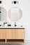 A bathroom detail with a wood floating cabinet and gold circular mirror.