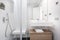 Bathroom with tiled shower in white tones with wooden cabinet and white washbasin