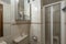 Bathroom with white porcelain fixtures, frameless mirror on the wall, and square walk-in shower with double-pane screen