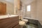 Bathroom with wooden furniture, porcelain sinks, shower column in the bathtub and green tiles on the floor