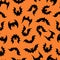 Bats vector seamless pattern. A flock of flying predators on an orange background. Black silhouettes of night bloodsuckers. Hand-