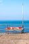 A battered red painted bench on the promenade with the sea and blue sky behind