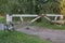 Battered, shabby white metal barred barrier that blocked passage along a country road strewn with small gray rubble.