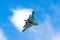 Battle fighter jet aircraft flying dives breaking clouds on a blue sky.