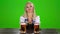 Bavarian girl sitting at a table with two glasses of beer. Green screen. Slow motion