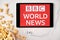 BBC World News logo on the screen of the tablet laying on the white table and sprinkled popcorn on it. Apple earphones