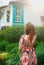BBeautiful young red-haired woman in a bright dress standing in nature, looking at the windows