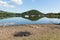 BBQ ashes by beautiful lake on calm idyllic summer morning with cloud reflections