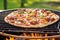 bbq pizza on a grill with flames licking the pizza stone