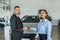 bbusiness client shaking hands with sales agent in suit after buying a car in showroom