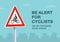 Be alert for cyclists on or crossing road sign. Close-up view.