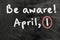 Be aware on blackboard note over a dark background. april fools day