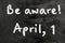 Be aware on blackboard note over a dark background. april fools day