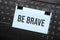 Be brave inscription on white paper note on laptop keyboard. Closeup message