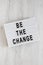 `Be the change` words on a lightbox on a white wooden background, top view. Overhead, from above, flat lay