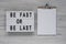 `Be Fast or Be Last` on a lightbox, clipboard with blank sheet of paper on a white wooden surface, top view. Flat lay, overhead,