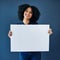 Be the first to know. Studio shot of a young woman holding up a blank placard against a blue background.