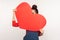 Be my Valentine! Positive happy young woman peeking out of big red paper heart with playful flirtatious look