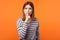 Be quiet! Portrait of serious woman with brown hair in long sleeve striped shirt. indoor studio shot isolated on orange background