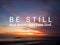 `Be still. And know that I am God.` Bible verse Psalm 46:10 on colorful sunset sunrise sky clouds background over the sea horizon.