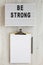 `Be strong` words on a lightbox, noticepad with blank sheet of paper on a white wooden background, top view. Overhead, from abov