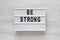 `Be strong` words on a lightbox on a white wooden background, top view. Overhead, from above, flat lay