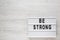 `Be strong` words on a lightbox on a white wooden background, top view. Overhead, from above, flat lay. Space for text