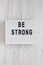 `Be strong` words on a lightbox on a white wooden surface, top view. Overhead, from above, flat lay