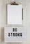 `Be strong` words on a modern board, noticepad with blank sheet of paper on a white wooden background, top view. Overhead, from